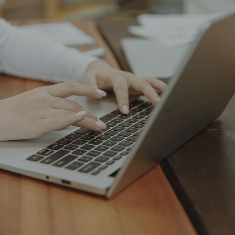 Newsletter Junge Hände tippen auf der Tastatur eines Laptops auf einem Holztisch.