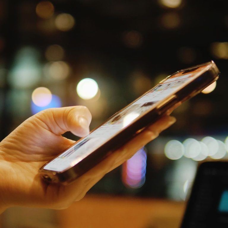 social media Eine Hand hält ein Smartphone mit hellem Bildschirm bei schwachem Licht.